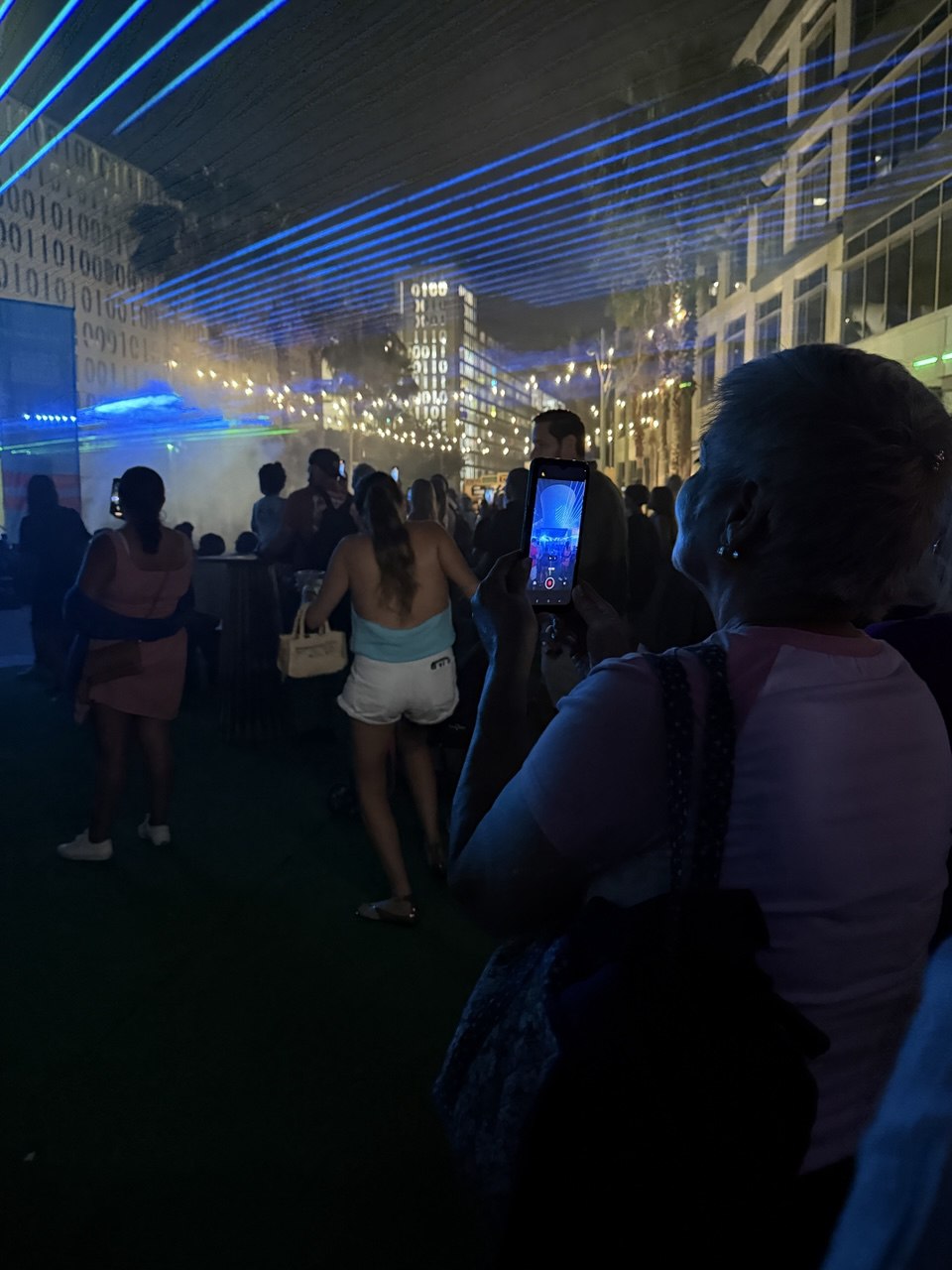 Audience member filming blue laser beams cutting through fog at Lake Nona Town Center